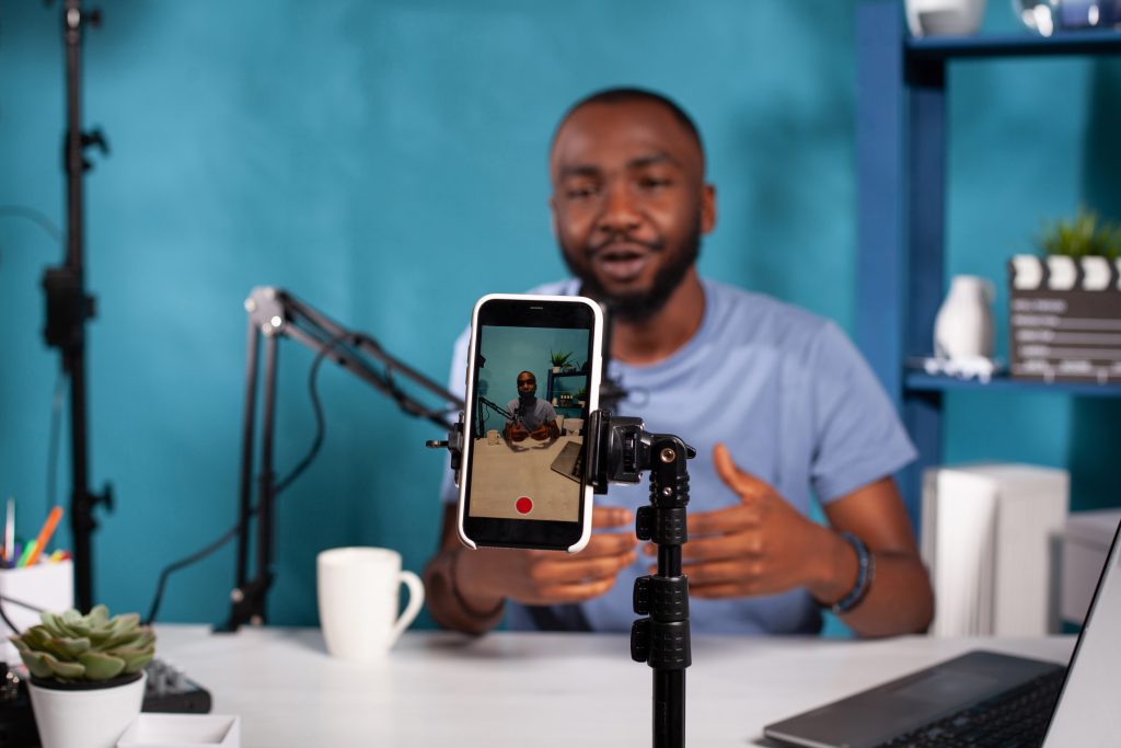 closeup of smartphone filming influencer sitting down at desk with laptop smiling